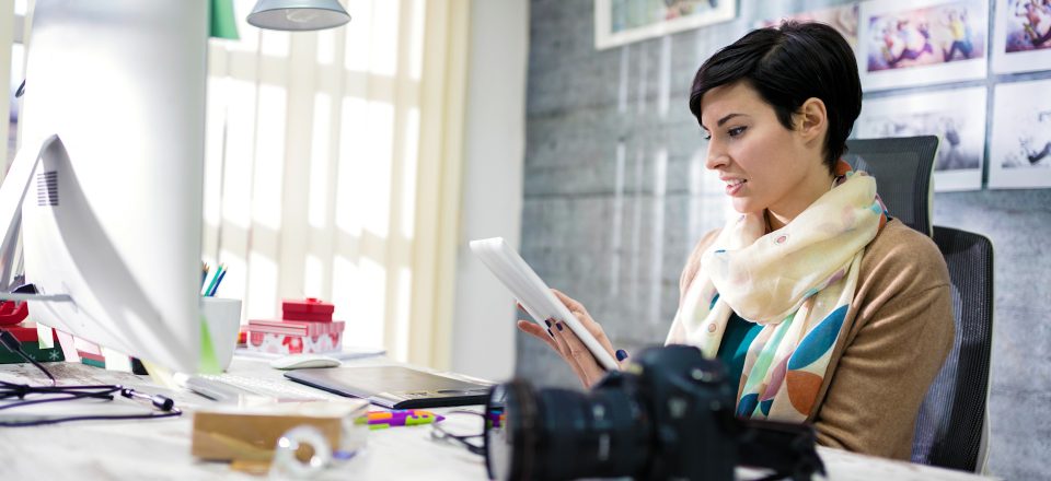 Woman in office woman-with-scarf-sitting-at-desk-searching-for-something-on-her-tablet